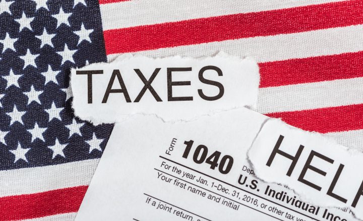 1040 tax form with word taxes in torn paper on American Flag and the word help.